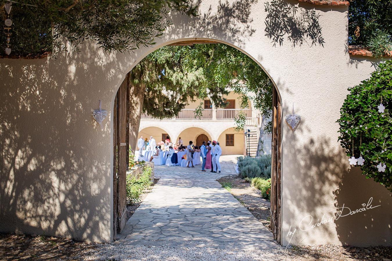 Wedding guests photographed through the Minthis Hills monastery gate, moments captured at a wedding at Minthis Hills in Cyprus, by Cristian Dascalu.