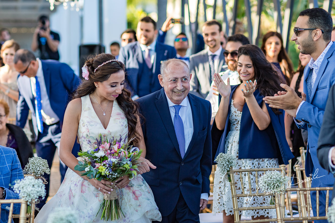 The bride coming down the isle with her father photographed during the ceremony, as part of an Exclusive Wedding photography at Grand Resort Limassol, captured by Cyprus Wedding Photographer Cristian Dascalu.