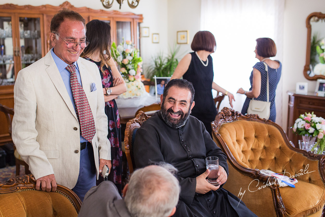 The priest, laughing and joking with wedding guests at the groom's house, captured at a wedding in Cyprus by Photographer Cristian Dascalu.